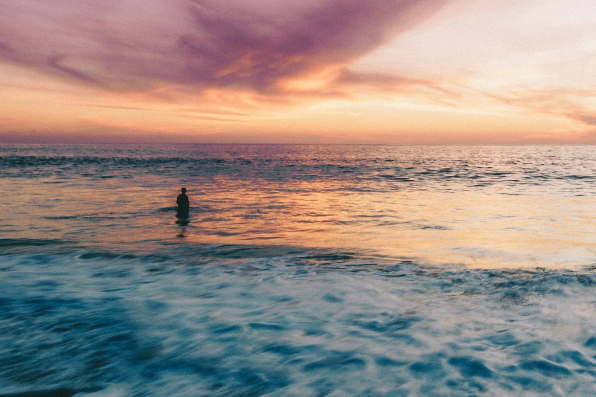 person standing on blue ocean water during orange sunset
